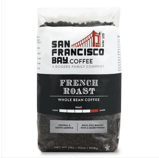 A bag of San Francisco Bay French Roast Whole Bean Coffee on a rustic wooden table with a steaming cup